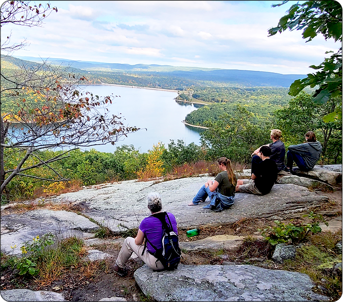 Hikers sitting at a rocky viewpoint enjoying the view of a lake and the mountains in the distance
