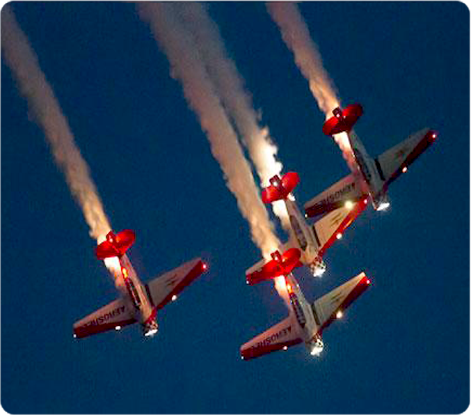 Four aerobatic planes with lights and smoke in delta formation finishing a loop at an airshow